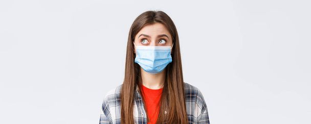 Coronavirus outbreak, leisure on quarantine, social distancing and emotions concept. Close-up of thoughtful, young woman in medical mask, look upper left corner reading sign or have bubble thought. - Foto, Imagem