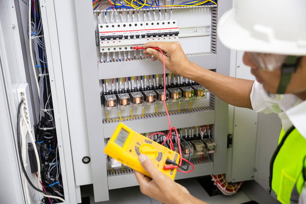 Electrician engineer work tester measuring voltage and current of power electric line in electical cabinet control. - Photo, Image