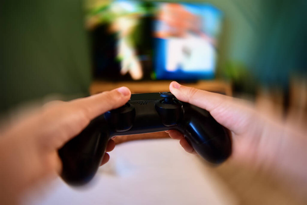 Jongen speelt videospel op console met joyctick gamepad in zijn hand, bewegingsvervaging effect. Online entertainment en vrijetijdsbesteding. Gokverslaving - Foto, afbeelding