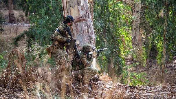 Twee airsoft spelers verstopten zich achter een boom en schoten op de vijand die elkaar dekte. Twee mannen met wapens in camouflage verbergen zich achter een boom.. - Foto, afbeelding