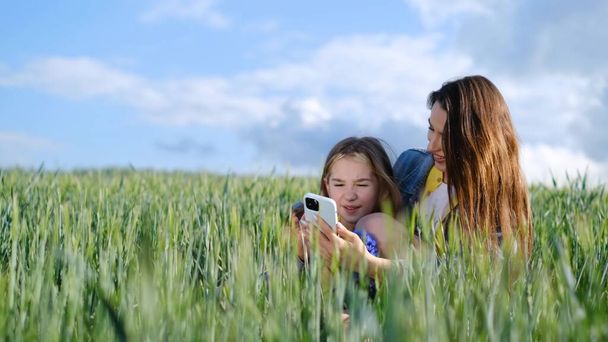 Happy family and children are resting. Mother and daughter walk in a green field of young wheat. Children run on the green fresh grass in a field in the countryside - Фото, изображение