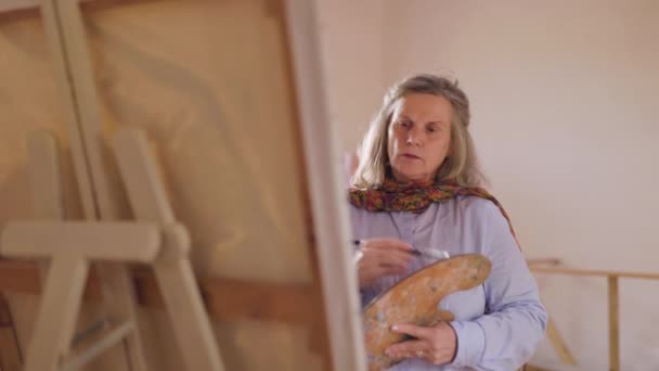 Érett művész nő nézi munkáját folyamatban, ahogy fejleszti hobbiját műhelyében - Felvétel, videó
