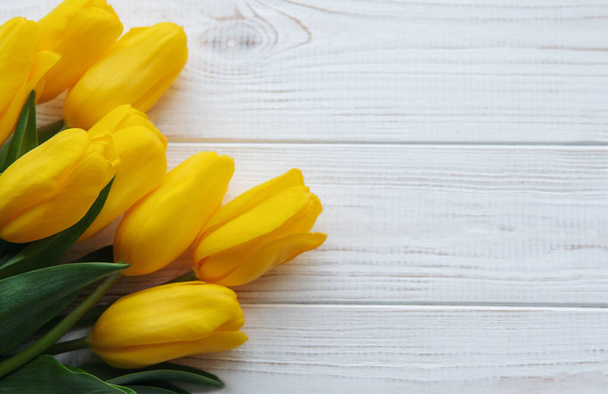 Delicados tulipanes amarillos sobre fondo de madera blanca. Vista superior, espacio para texto, borde - Foto, imagen