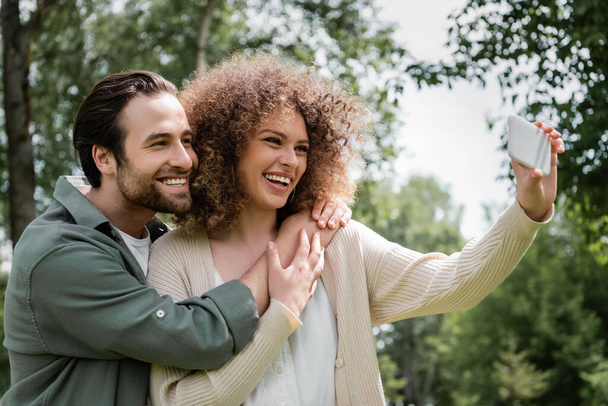 positiivinen nuori pari ottaa selfie matkapuhelimeen kesäpuistossa - Valokuva, kuva