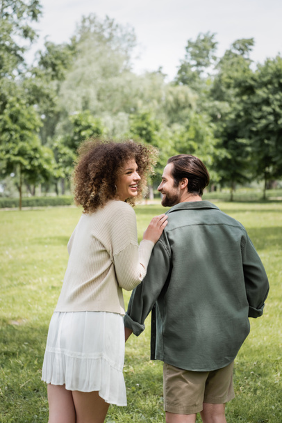 curly woman in dress and man in summer clothes having date in park - Фото, изображение