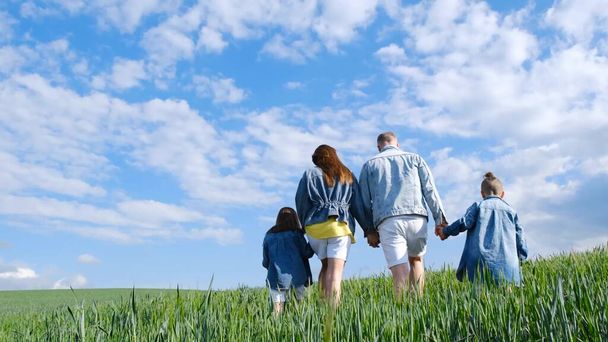 Cheerful family walks through a green field of wheat. Parents hold children by the hands. Family running outdoors. Happy family spending time together - Фото, зображення