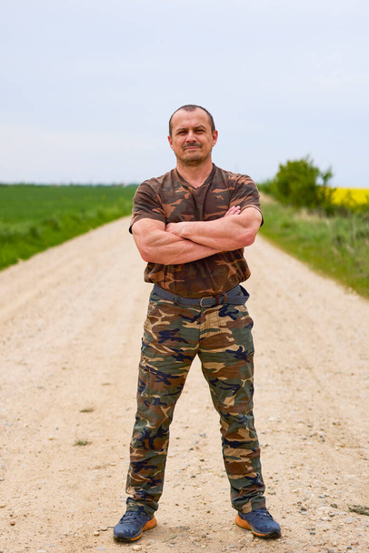 A man standing with his hands folded on an agricultural road. - Valokuva, kuva