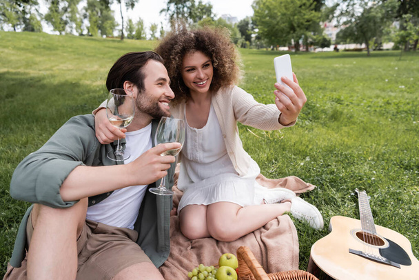счастливая молодая пара делает селфи на смартфоне во время летнего пикника в парке  - Фото, изображение