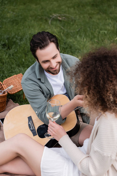 high angle view of romantic man playing acoustic guitar near curly woman with glass of wine  - Photo, Image