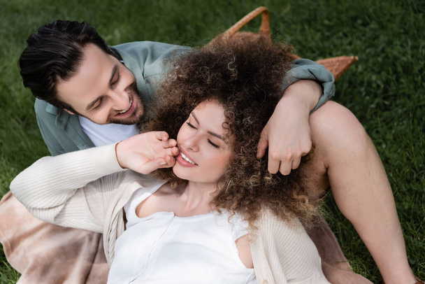 top view of curly woman lying on happy boyfriend during picnic in summer park  - Foto, Imagem