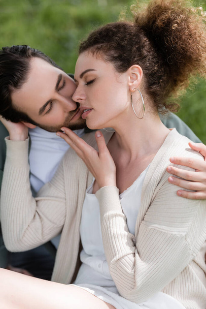 barbudo homem e encaracolado mulher abraçando e beijando no parque - Foto, Imagem