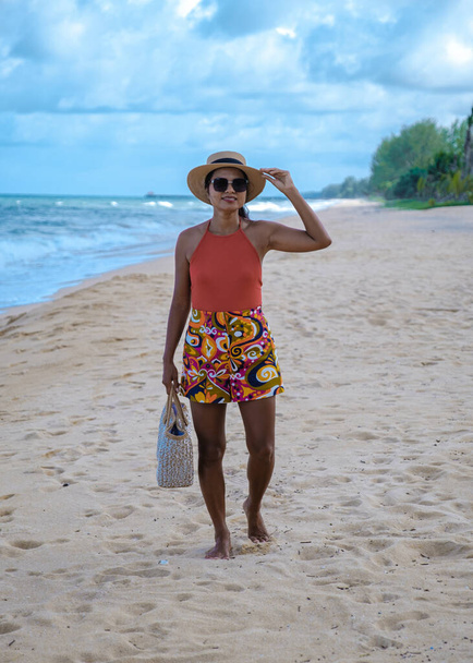 Azjatka elegancka kobieta spaceruje po plaży z kapeluszem i torbą.  - Zdjęcie, obraz