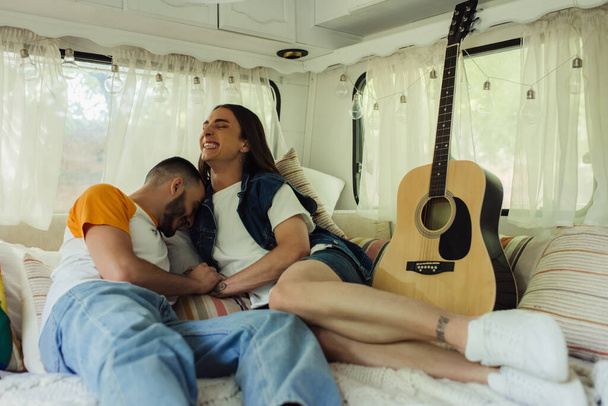 uśmiechnięty gej człowiek z tatuaże śmiech z brodaty chłopak na łóżko w nowoczesny van  - Zdjęcie, obraz