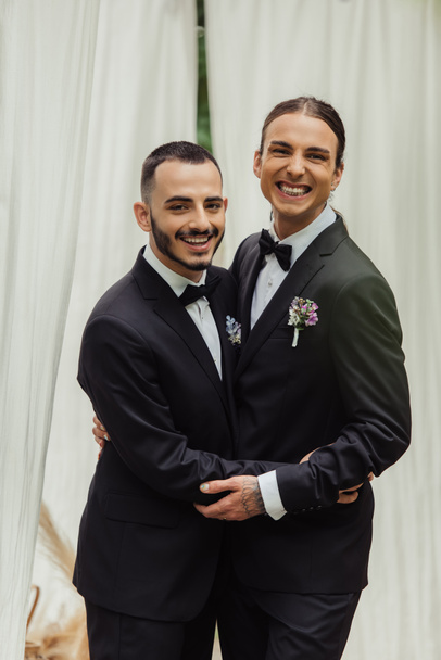 happy gay couple in suits with boutonnieres hugging during wedding ceremony  - Photo, Image