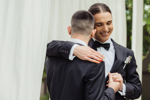 happy gay couple in suits holding hands and hugging on wedding day - Foto, Imagem