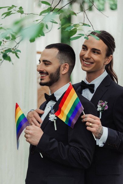 felice gay sposi in formale usura con boutonnieres holding lgbt bandiere  - Foto, immagini