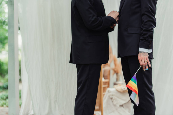 partial view of tattooed gay man with wedding ring holding lgbt flag near groom  - Fotoğraf, Görsel