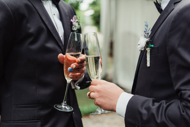 recortado vista de gay recién casados en trajes celebración copas con champán en el día de la boda  - Foto, Imagen