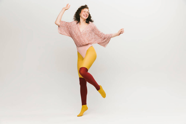 Dancing. Portrait of young beautiful astonished girl in avant-garde style over white background. Stylish model in bright yellow tights. Vivid style, beauty, queer, freak, fashion concept. - Photo, Image
