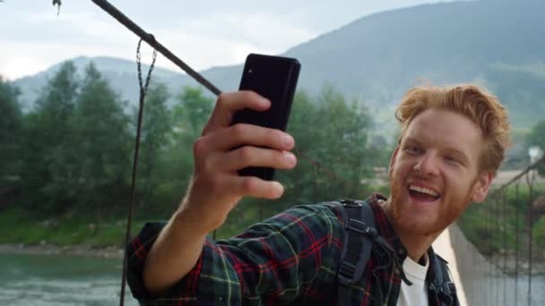Lachende toerist neemt selfie foto op smartphone. Energetische wandelaar poseren mobiele telefoon camera in de bergen brug natuur van dichtbij. Gelukkige man verken de wereld. Reiziger die mobiel wandelt. Reisconcept. - Video