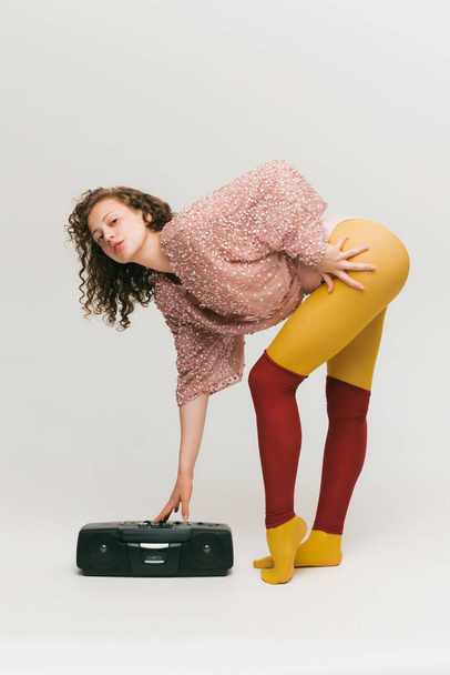 Retro music. Portrait of young beautiful astonished girl in avant-garde style over white background. Stylish model in bright yellow tights. Vivid style, beauty, queer, freak, fashion concept. - Photo, image