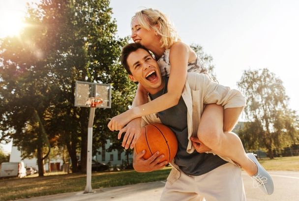 summer holidays, love and people concept - happy young couple with ball having fun on basketball playground - Zdjęcie, obraz