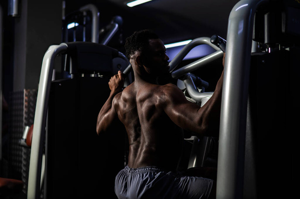 Shirtless african american man doing back exercises on a machine in the gym - 写真・画像