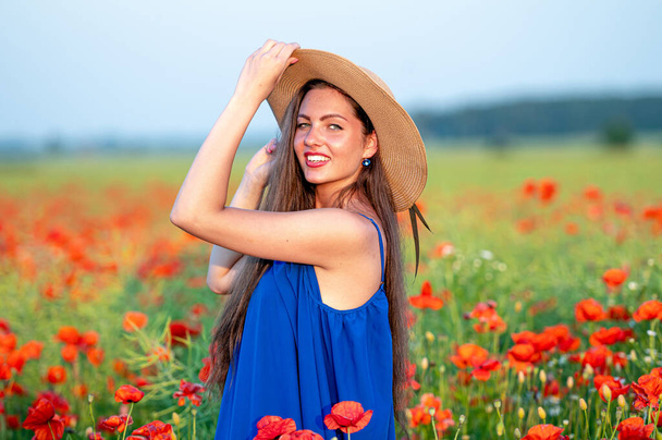 portrait of elegant young woman with long hair and straw hat in poppy field in evening sunlight - Foto, immagini