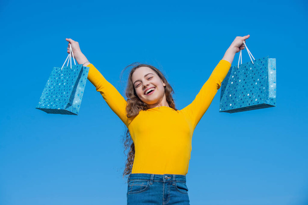 positive teen girl with shopping bags, blue yellow. - Foto, afbeelding