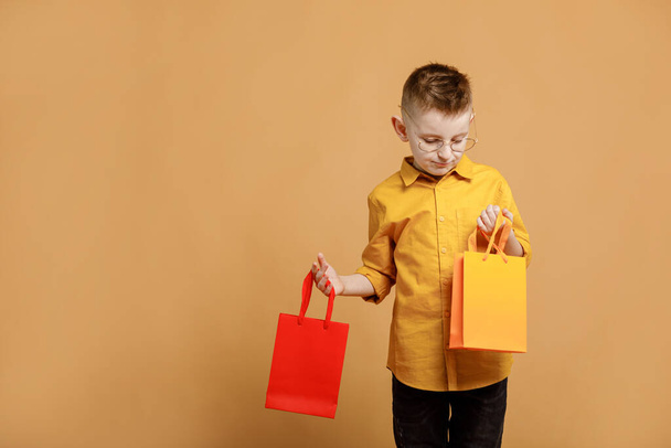 Shopping on black friday. Little boy holding shopping bags on yellow background. Shopper with many colored paper bags. Holidays sales and discounts. Cyber monday. High quality photo. - Zdjęcie, obraz