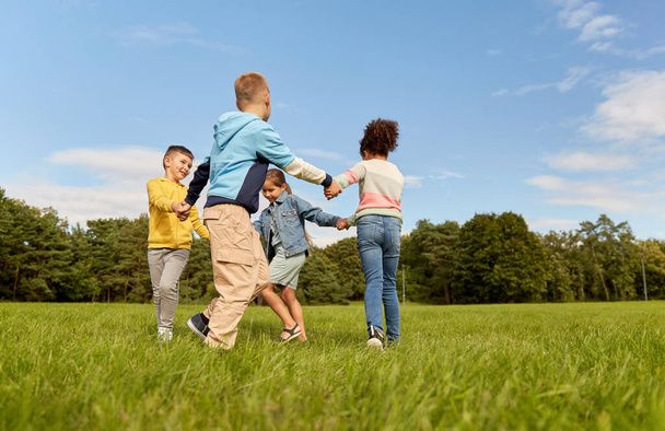 childhood, leisure and people concept - group of happy kids playing round dance at park - Fotoğraf, Görsel