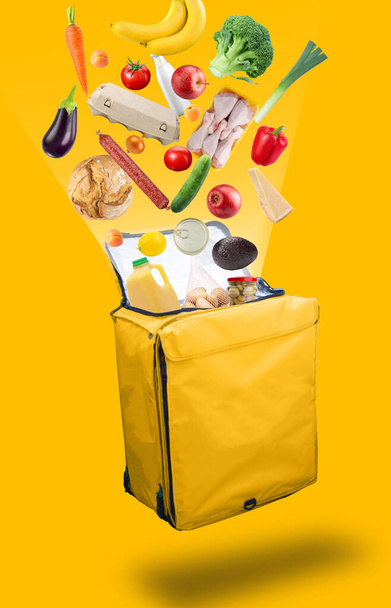 Warzywa, produkty, które wylatują z otwartej żółtej torby dostarczającej żywność kuriera, izolowane na żółtym tle. Koncepcja dostarczania świeżej żywności. - Zdjęcie, obraz
