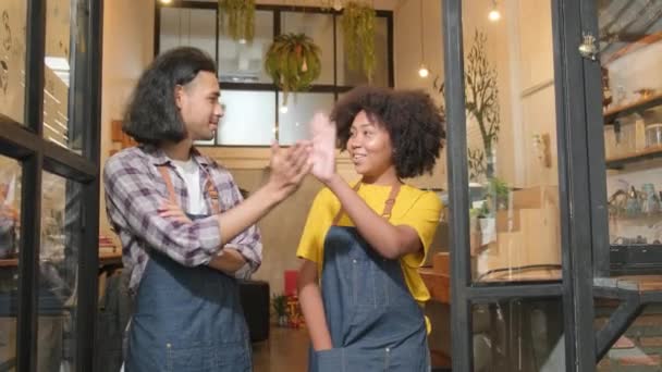Two young startup barista partners with aprons stand at casual cafe door, arms crossed, laugh and tease together, happy and cheerful smiles with coffee shop service jobs, small business entrepreneurs. - Záběry, video