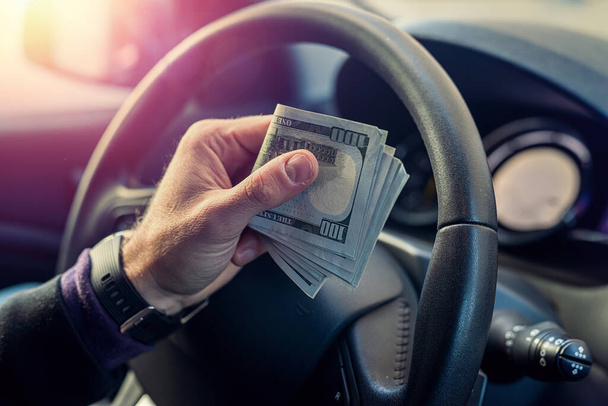 young man in his own cool car calculates the salary in dollar bills. Business concept. The concept of a driver in a car - Photo, Image