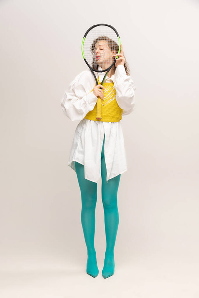Tennis time. Portrait of young beautiful astonished girl in avant-garde style over white background. Stylish model in bright yellow tights. Vivid style, beauty, queer, freak, fashion concept. - Photo, image
