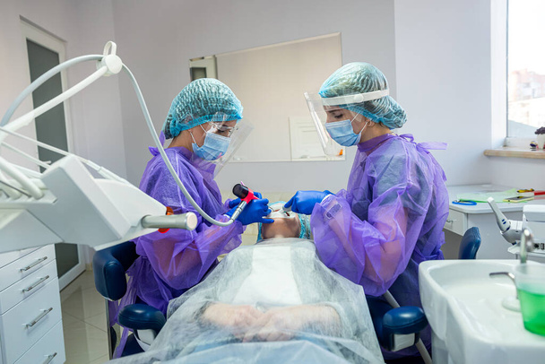 Özel kıyafet maskeli iki güzel yardımcı eldiven dişçiye ameliyat için yardımcı olur. Diş cerrahisi kavramı - Fotoğraf, Görsel