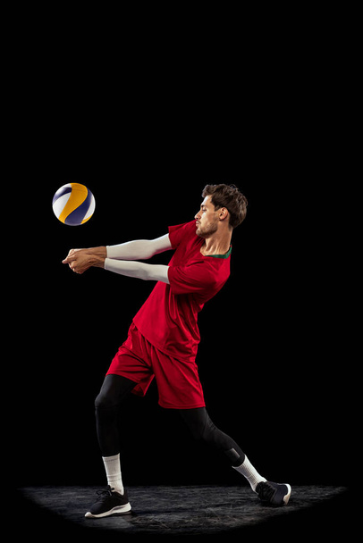 Portrait of young concentrated man, volleyball player in motion, training, playing isolated over black studio background. Concept of sport, action, team game, active lifestyle, health, hobby, ad - Photo, Image