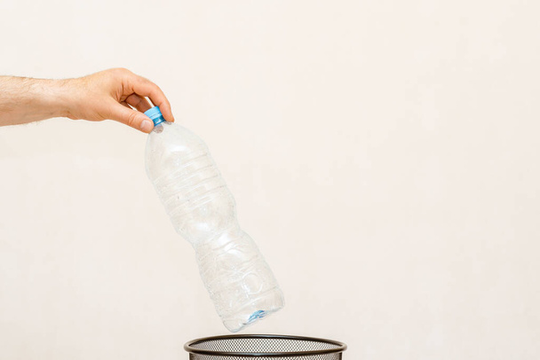 La botella de plástico se arroja a la cesta de la basura para su eliminación y reciclaje. fondo blanco, gris, enfoque selectivo, espacio de copia. - Foto, imagen