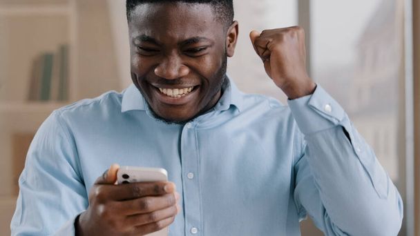 Африканский молодой человек удивлен получить хорошее сообщение на мобильный телефон выиграть онлайн ставку радоваться прохождения уровня мобильной игры мужчина американский парень бизнесмен испытывает шок да жест отпраздновать победу в Интернете - Фото, изображение