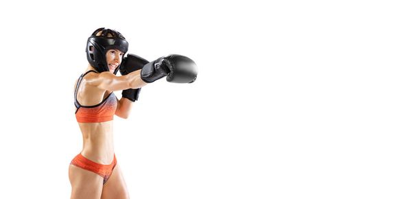 Portrait of young female professional kickboxer in sports gloves and protective helmet in motion isolated on white background. Sport, competition, power concept. Flyer for ad - Photo, Image