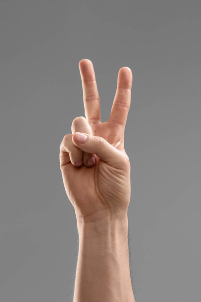 gesture, count and people concept - close up of male hand showing peace over grey background - Фото, зображення