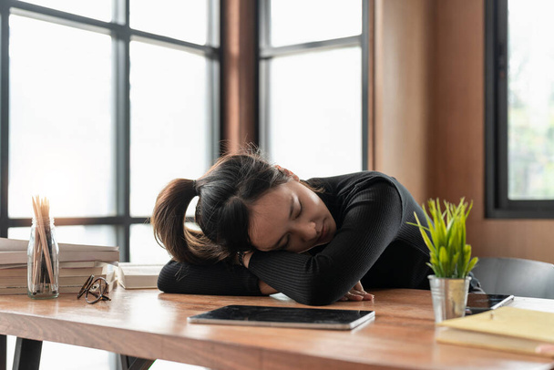 Измученная, напряженная азиатская молодая деловая женщина, работающая, сняла очки с напряжением глаз, вздремнула, поспала на столе после тяжелой работы, используя ноутбук, офисный синдром. Овертайм, уставшие люди. - Фото, изображение