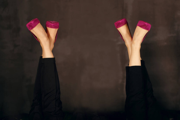 Zwei Paar Frauenbeine in fliederfarbenen Schuhen auf dem Kopf vor dunklem Hintergrund. Frauenbeine in hellen Schuhen mit Freiraum für Text. Modebild mit Frauenbeinen und lila Schuhen - Foto, Bild