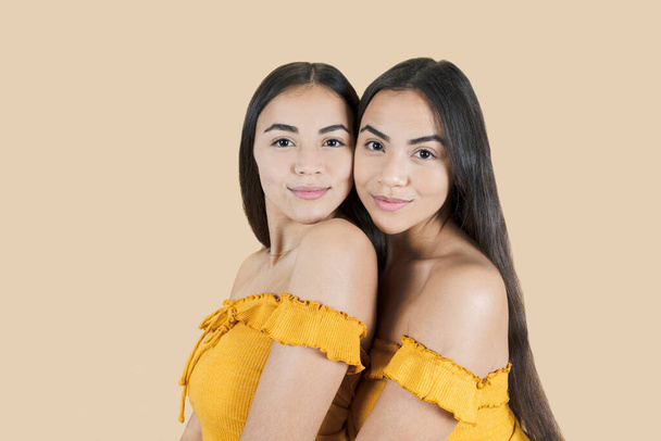 hermanas gemelas belleza beige fondo, retrato de hermosas hermanas jóvenes de pie contra fondo de color - Foto, imagen