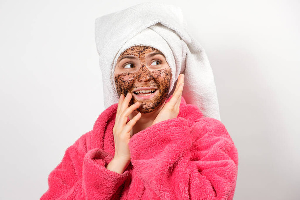 Uma mulher faz uma limpeza facial a partir de grãos de café e olha para o lado, copiando o espaço para o texto - Foto, Imagem