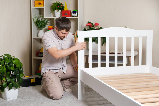The father assembles the children's bed for the child, the man twists the screws into wooden furniture - Photo, image