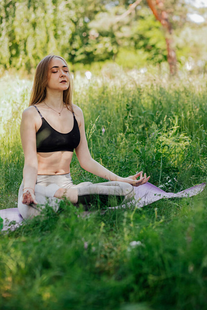 Yoga woman on green grass girl relaxes in the field. Yoga woman in green park girl doing gymnastics outdoors. Meditating woman in meditation in yoga pose practices outdoors - Fotoğraf, Görsel