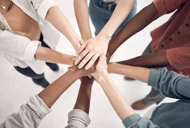Group of diverse businesspeople piling their hands together in an office at work. Business professionals having fun standing with their hands stacked for support and unity from above. - 写真・画像