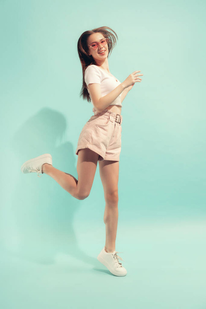 Jumping. Excited young beautiful girl with long hair posing isolated on light blue color background. Concept of beauty, art, fashion, emotions, youth. Copy space for ad - Foto, Imagem