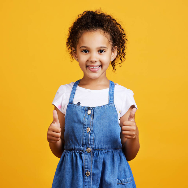 Stúdió portré vegyes verseny lány így hüvelykujját elszigetelt sárga háttér. Aranyos spanyol gyerek pózol odabent. Boldog és aranyos gyerek ad támogatást, hogy pozitív és gesztus, egyetértek. - Fotó, kép